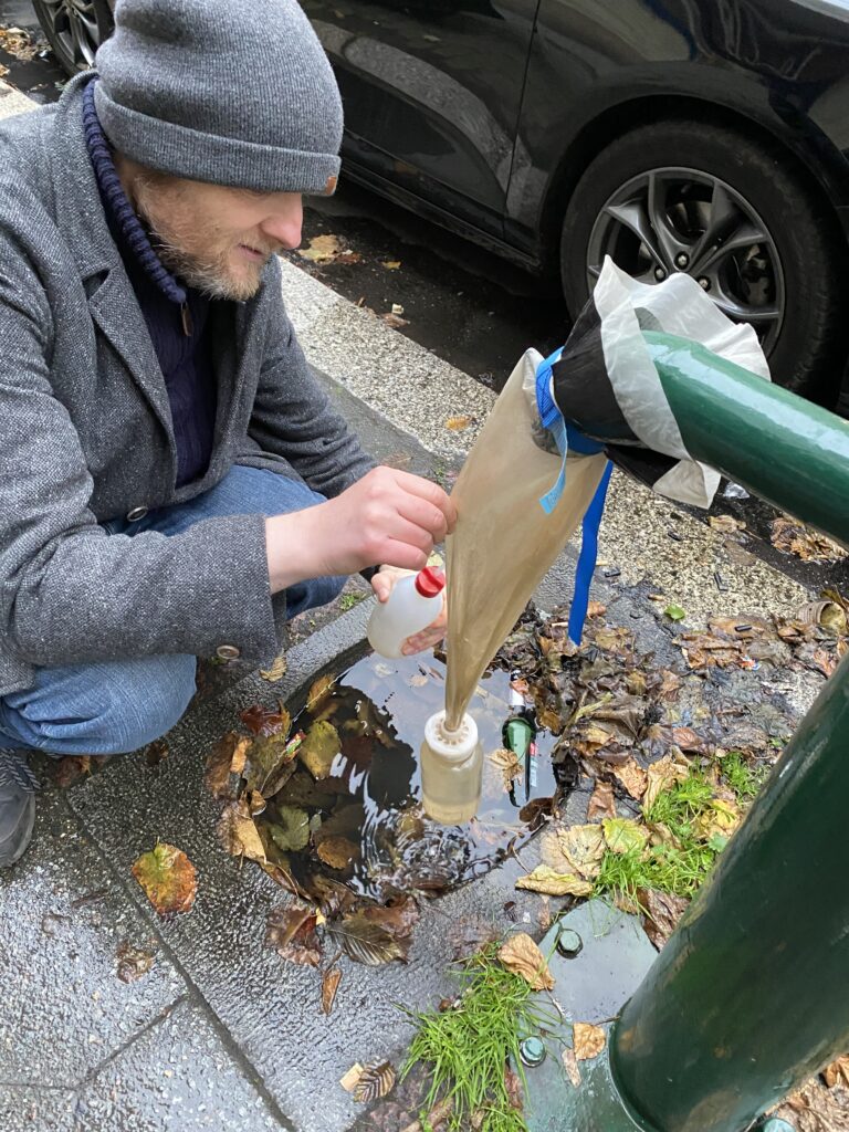 Ein Mann spült das Filternetz, in dem Kleinstlebewesen aus dem Grundwasser aufgefangen werden, aus, um alle Tierchen in die daran hängende Probeflasche zu bekommen.